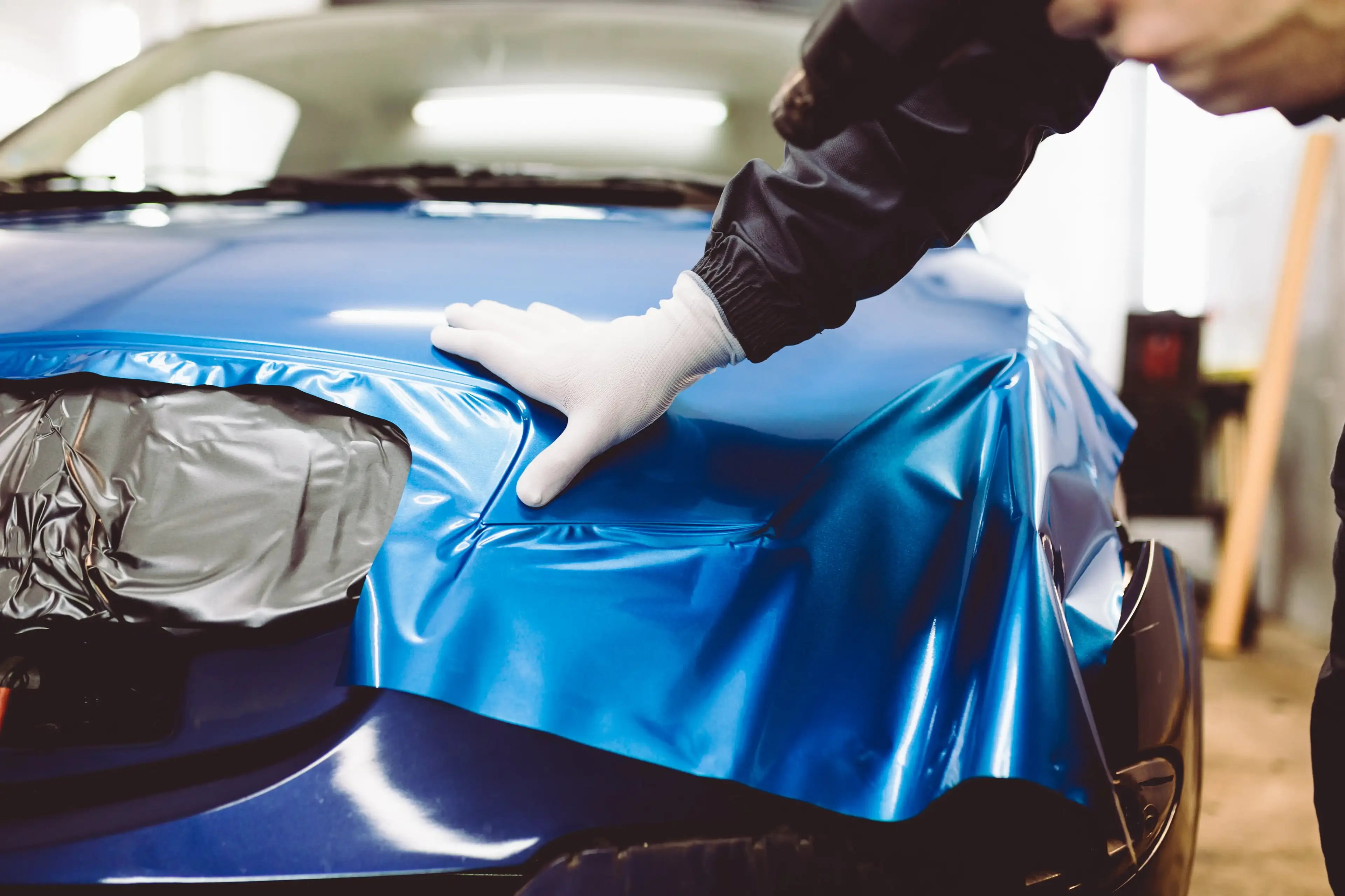 Technician applying a blue vinyl wrap to a car’s hood, demonstrating the process of customizing a vehicle’s appearance with precision.