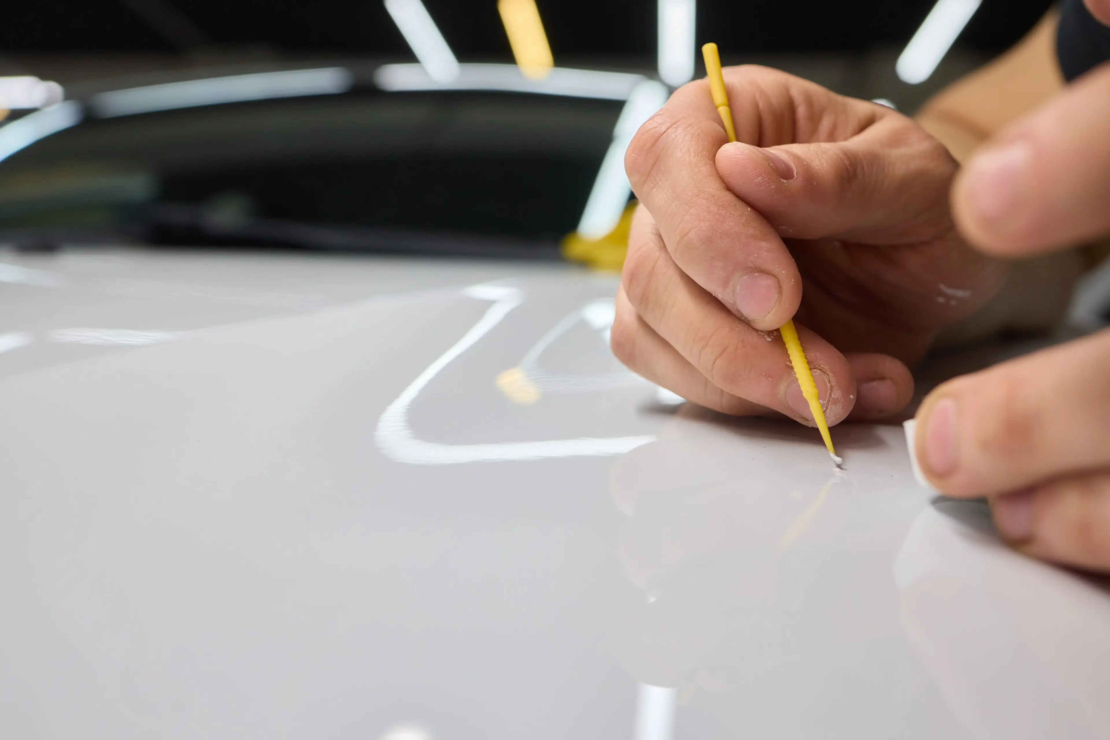 Close-up of a technician carefully repairing a scratch on a car’s surface with precision tools, showcasing meticulous paint correction work.