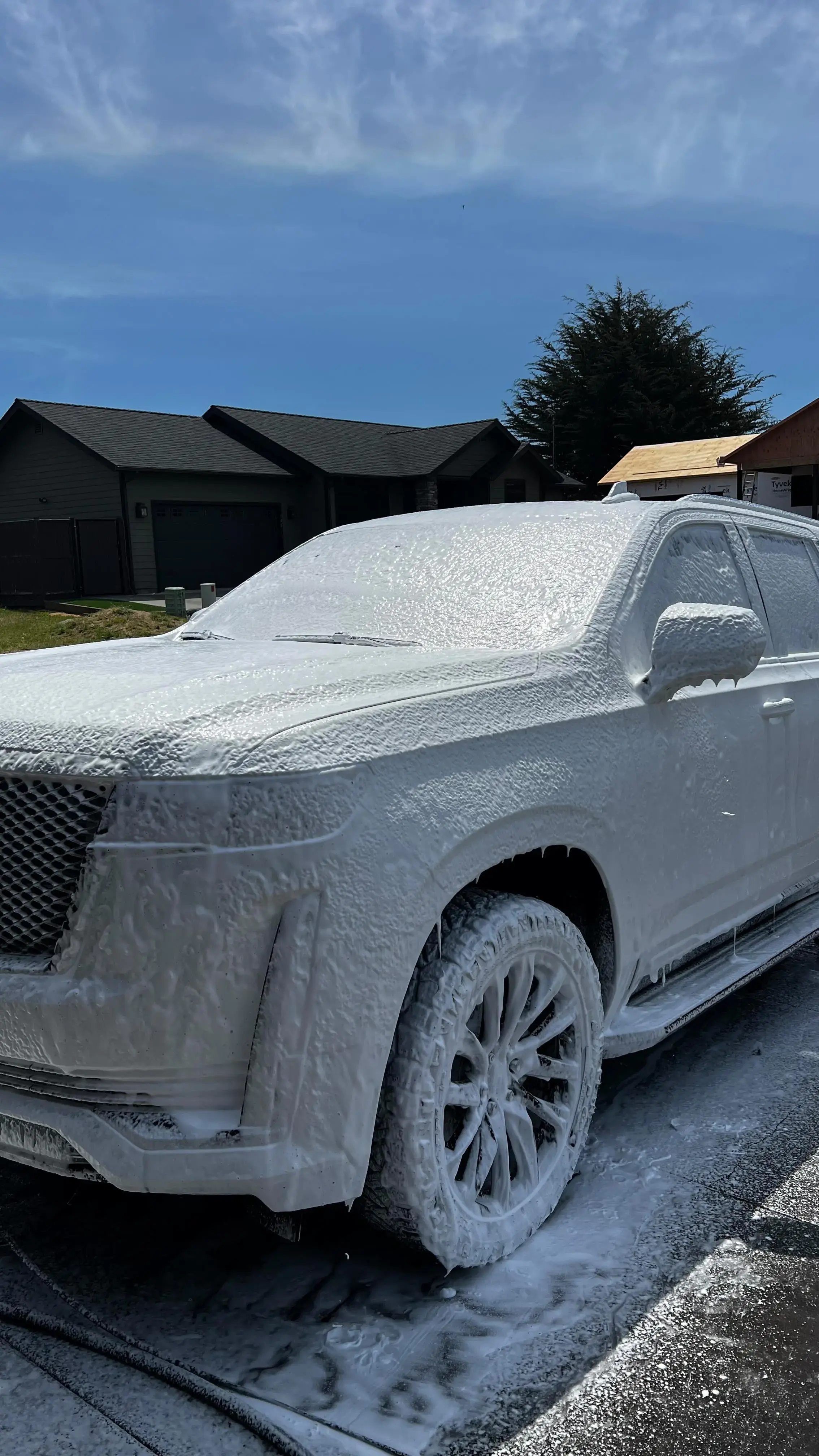 A car completely covered in foam during a thorough exterior wash, preparing for a detailed cleaning.